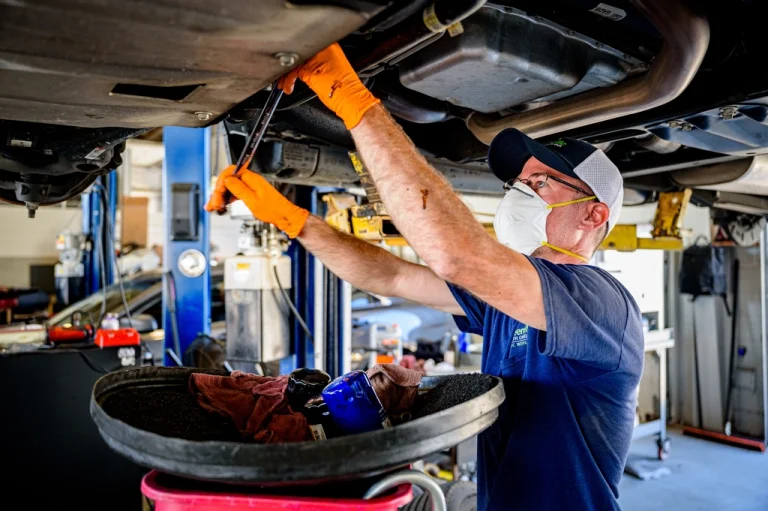 Technician draining engine oil from underneath a car during an interim service