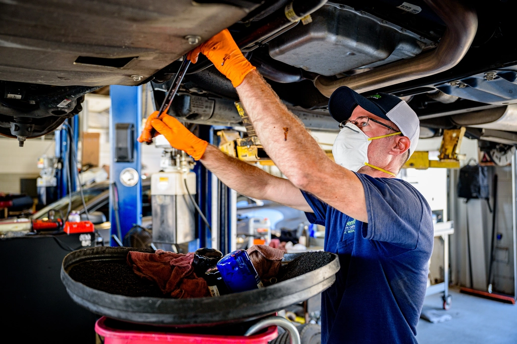 Technician draining engine oil from underneath a car during an interim service